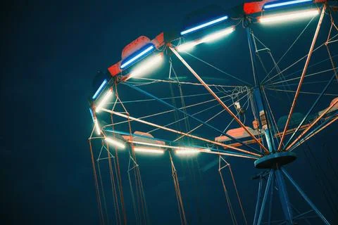 Empty chain swing ride lit with bright LED lights during evening twilight. Stock Photos