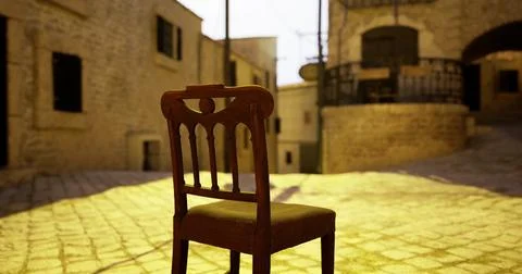 Empty chair under warm sunlight in a historic stone street Ilustración de archivo
