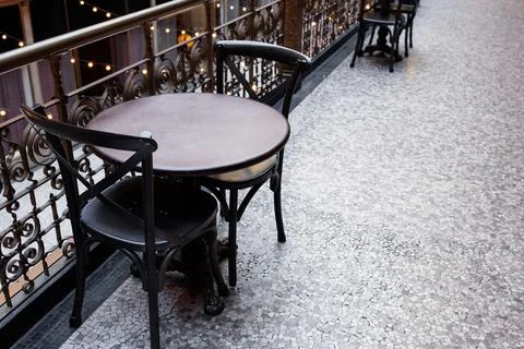 Empty chairs and tables on a balcony with iron railing and stone floor duri.. Stock Photos