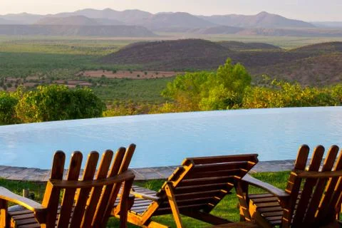 Empty chairs by the swimming pool overlooking the African savannah landscape Stock Photos