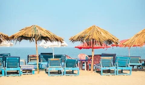 Empty chairs under thatched umbrellas on a sandy beach in Goa Stock Photos