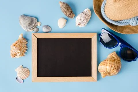 Empty chalkboard with seashells, hat and glasses on blue background. Stock Photos