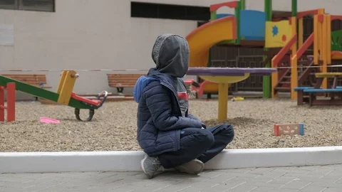Empty children's playground. Boy sitting near the playground. He's bored Stock Footage 130117893