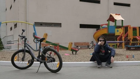 Empty children's playground. Boy sitting near the playground. He's bored Stock Footage 130117936