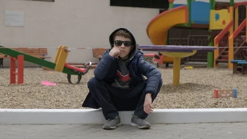 Empty children's playground. Boy sitting near the playground. He's bored Stock Footage 130117949