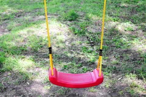 Empty children's red plastic swing on yellow ropes. Childhood and loneliness Stock Photos