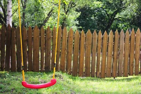 Empty children's red plastic swing on yellow ropes. Childhood and loneliness Stock Photos