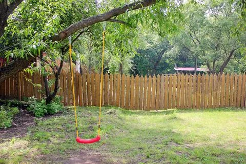 Empty children's red plastic swing on yellow ropes. Childhood and loneliness Stock Photos