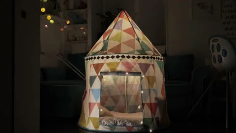 An empty children's tent illuminated by lanterns stands in a dark living room Stock Footage 235437846