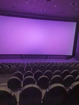 Empty cinema auditorium with rows of seats and projector screen in purple tone Foto stock