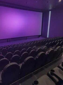 Empty cinema auditorium with rows of seats and projector screen in purple tone Foto stock
