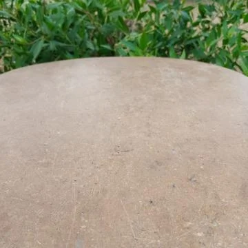 Empty circular curved brown stone table top surface with blurred foliage Фото