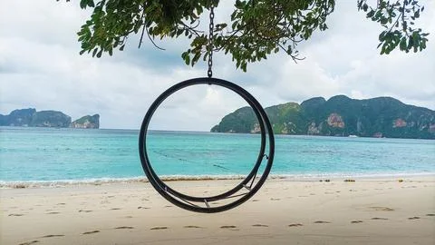 Empty circular swing on a sandy beach under a cloudy sky 库存照片