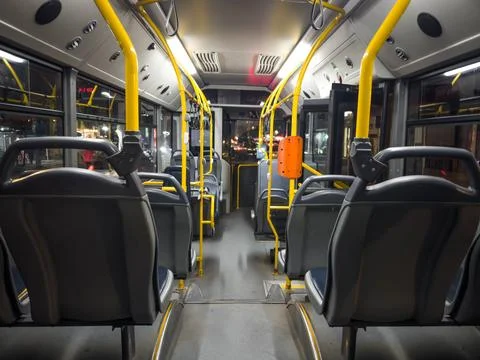 Empty city bus interior at night with modern seats and yellow handrails, urba Stock Photos