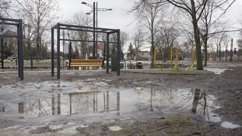 Empty city park with mud and bench swing reflected in puddles during spring thaw Stock Footage 329640180