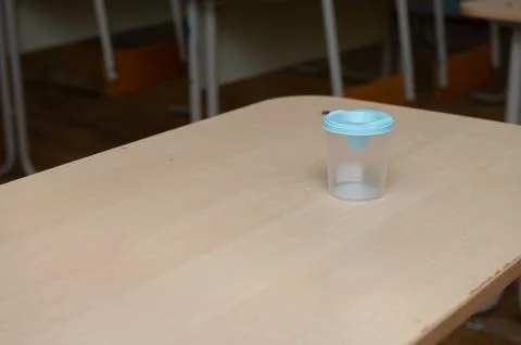 Empty classroom desk with blue-topped plastic cup on wooden table Stock Photos