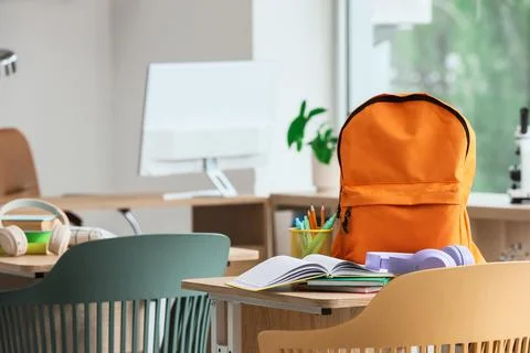 Empty classroom desk with orange backpack, open notebook, and school supplies Stock Photos