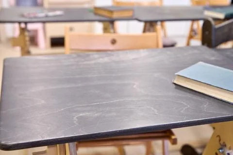 Empty classroom desk with single closed book on black laminated surface Stock Photos