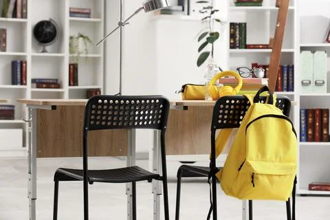 Empty classroom desk with yellow backpack, headphones, and books, ready for l Stock Photos