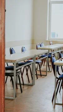 An empty classroom with rows of desks and blue chairs in a bright, academic s Stock Photos
