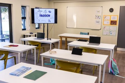 Empty classroom showing white tables, mustard chairs, laptops, tablet, monitor Stock Photos