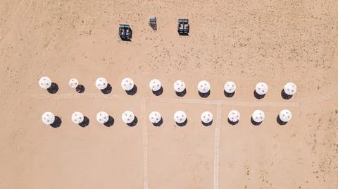 An empty clean sandy beach with two rows of parasols and cabanas, aerial view. Stock Photos
