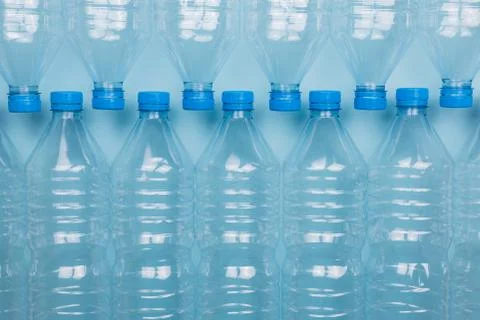 Empty clear plastic bottles with caps stacked on a blue background. Recycling Foto stock