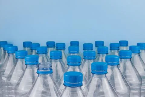 Empty clear plastic bottles with caps stacked on a blue background. Stock Photos