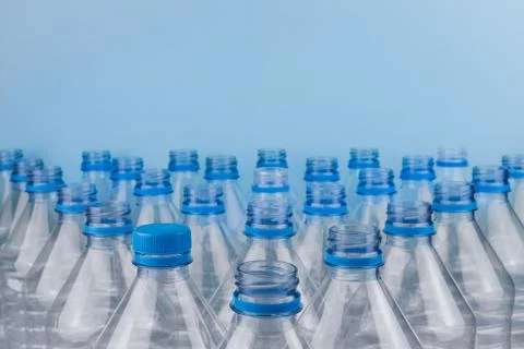 Empty clear plastic bottles with caps stacked on a blue background. Stock Photos
