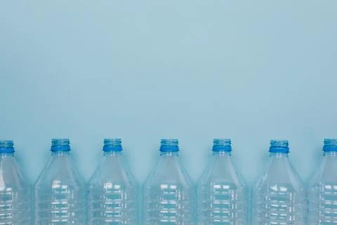 Empty clear plastic bottles without caps stacked on a blue background. Recycl Stock Photos