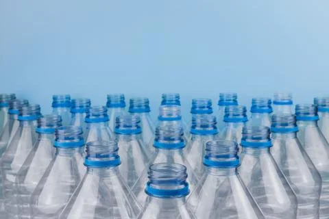 Empty clear plastic bottles without caps stacked on a blue background. Recycl Stock Photos
