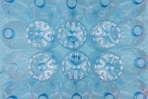 Empty clear plastic bottles without caps stacked on a blue background. Recycl Stock Photos