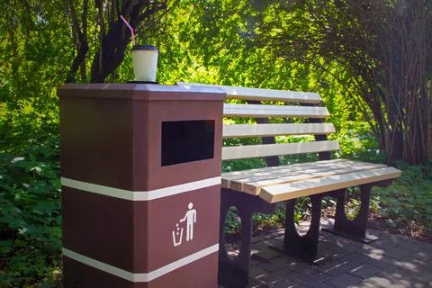 Empty coffee cup with straw on trash can near park bench on background of grass Stock Photos