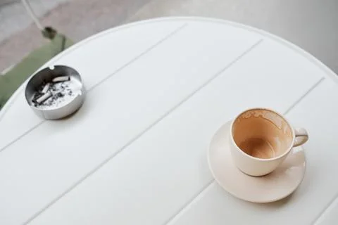 Empty coffee cup on a white table with an ashtray nearby. Minimal urban scene Stock Photos