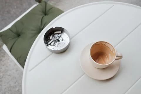 Empty coffee cup on a white table with an ashtray nearby. Minimal urban sce.. Stock Photos