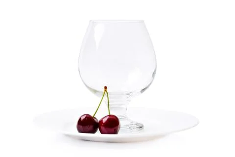 Empty cognac glass next to cherry berries on a white plate isolated on white  Foto stock