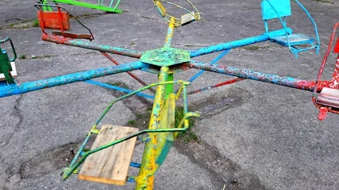 Empty colorful carousel spinning slowly on an old cracked playground Stock Footage 337654027