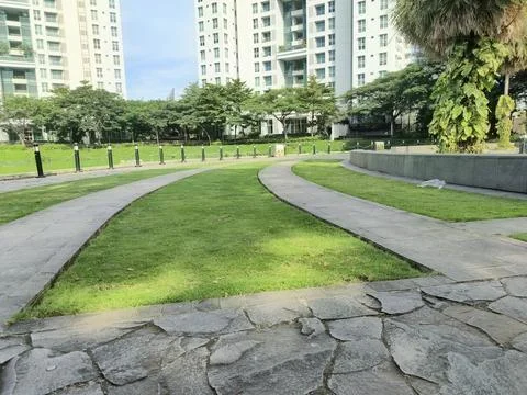 An empty concrete park bench sits at the edge of a green park path. The con.. Stock-Fotos