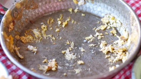 Empty copper pan with leftover scrambled eggs and crumbs on a red and white.. Video stock 333152027