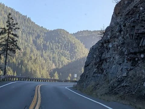 An empty country road bends through a wooded valley bordered by cliffs Photos