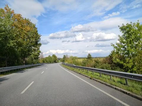 Empty country road curving between green deciduous trees under blue sky cloud Foto stock