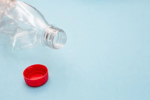 Empty crumpled plastic bottle and a red cap on blue background with place for Stock Photos