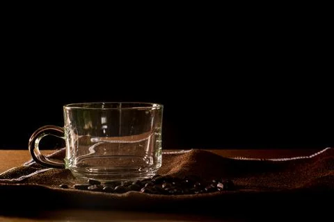 Empty cup and group of coffee beans on brown table cloth with black backgro.. Stock Photos