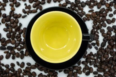 An empty cup with yellow inside on coffee beans background. Stock Photos