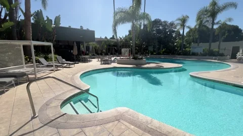 Empty curved resort swimming pool with loungers and cabanas among palm trees Stock Footage 345369803