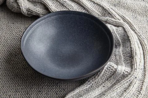 Empty dark plate on the background of a light knitted woolen sweater Stock Photos