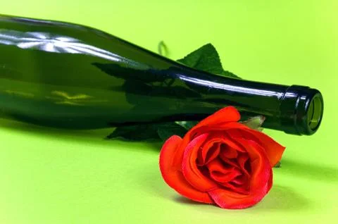 Empty dark wine bottle with red rose on green background, art Stock Photos