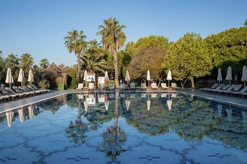 Empty deck chairs and folded parasols reflecting on swimming pool at resort Stock Photos