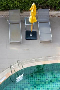 Empty deck chairs with closed parasol by the swimming pool at sunset. Stock Photos