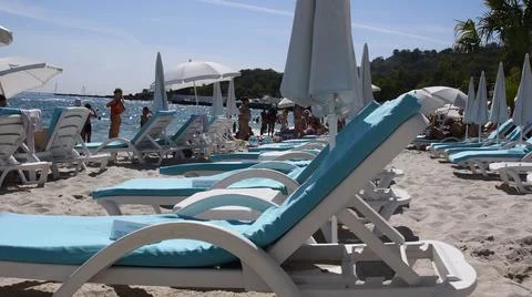 Empty deck chairs on white beach sand at seashore and suntanning people Stock Photos